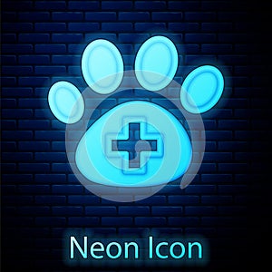 Glowing neon Veterinary clinic symbol icon isolated on brick wall background. Cross hospital sign. A stylized paw print