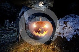 Glowing orange halloween pumpkin with scyry zombie hand on old graveyard front of full moon black raven church dark night spooky