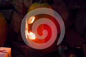 Glowing pumpkin on halloween night with candles on a background of firewood and autumn foliage