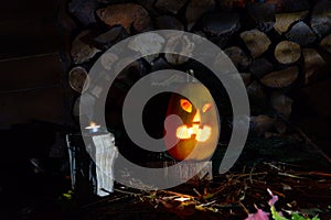 Glowing pumpkin on halloween night with candles on a background of firewood and autumn foliage