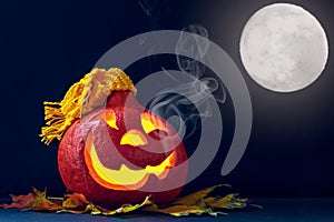 Glowing pumpkin in a hat with smoke and autumn leaves on a dark background. Jack`s Lantern. Halloween Decorations