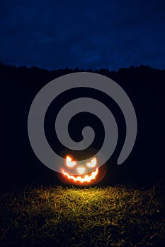 Glowing scary Halloween pumpkin on the grass at night.