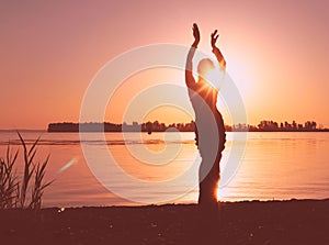 Glowing silhouette of slim woman with hands up in the air illuminated with sunshine