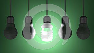 Glowing spiral light bulb among dead tungsten ones hanging on green