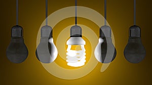 Glowing spiral light bulb among dead tungsten ones hanging on yellow