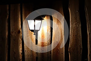 Glowing street lamp on the background of a wooden fence at night. Light permeates the darkness. Street lighting. Creating a cozy a