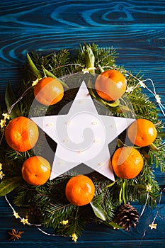 Glowing white LED star surrounded with fresh mandarins and spruce branches with garland lights.