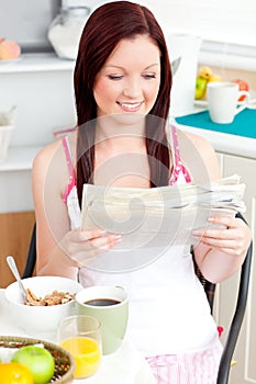 Glowing woman eating cereals and reading newspaper