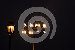 A glowing wrought-iron lamp on a lamppost and luminous industrial lamps at night  against the dark sky  illuminate with a contour