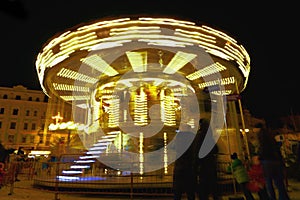Glowing yellow children`s carousel in motion, in the evening.