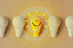 Glowing yellow light bulb with smile and white light bulb turned off - Positive thinking and standing out from crowd concept