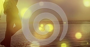 Glowing yellow spots of light against mid section of a woman walking on the beach