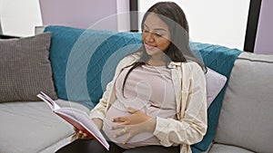 Glowing young pregnant woman enjoying comfortable rest, engrossed in reading book while touching belly and radiating positivity at