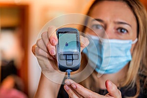 Glucometer device for glucose test with dripped blood in diabetic patients held by the blonde nurse with surgical mask photo