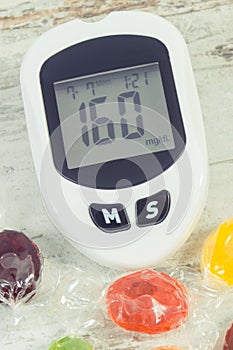 Glucometer with high sugar level and candies. Healthy lifestyle, nutrition and reduction eating sweets during diabetes