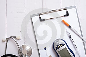 Glucometer, stethoskope and syringes with a tablet on a wooden background, top view. Treatment of diabetes concept