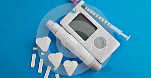 Glucometer with sugar cubes insulin test strips, lancet pen and syringe on blue background