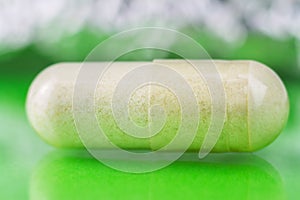 Glucosamine capsule, food supplement pills on glossy green background, macro image, soft blurred bokeh circles.
