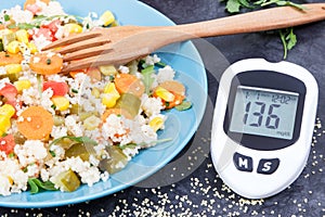 Glucose meter for checking sugar level and salad with vegetables and couscous groats. Light and healthy meal for diabetics