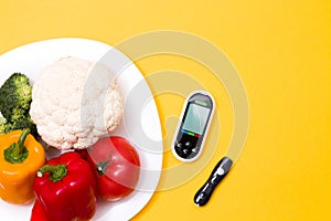 glucose meter and a needle on a yellow background, a white large plate with vegetables, copy space