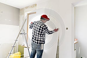 Glueing wallpapers at home. Young man, worker is putting up wallpapers on the wall. Home renovation concept