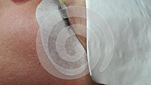 Gluing artificial eyelashes with tweezers. Cosmetic procedure. Eyelash extension. Woman eye with long eyelashes
