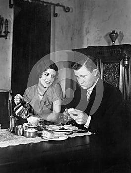 Glum man and adoring woman at breakfast table photo