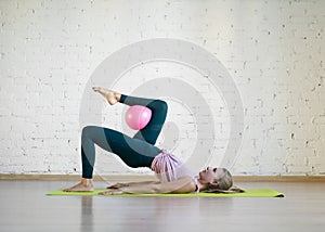 Gluteal bridge with pink small fit ball. Caucasian girl doing pilates with special equipment in fitness studio.