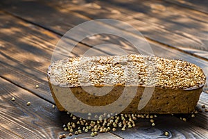 Gluten-free buckwheat bread with a golden brown crust, sprinkled with sesame seeds, lies on a wooden table. Healthy