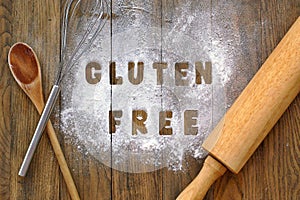 Gluten free flour with text gluten free in English language with wooden spoon, beater and rolling pin on dark brown wooden backgro