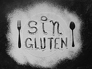 Gluten free flour with text gluten free in Spanish language with spoon and fork silhouette made with flour on dark texture