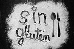 Gluten free flour with text gluten free in Spanish language with spoon and fork silhouette made with flour on dark texture photo