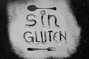 Gluten free flour with text gluten free in Spanish language with spoon and fork silhouette made with flour on dark texture photo