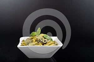 Gluten-free fresh cooked penne pasta from green peas isolated on black background, basil leaf top