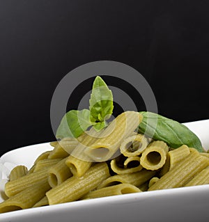 Gluten-free fresh cooked penne pasta from green peas isolated on black background, basil leaf top