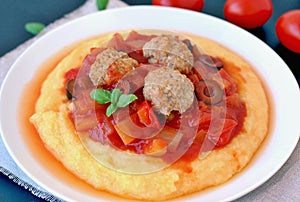 Gluten free meal from meatballs, vegetable ragout and polenta with tomato and basil on white plate on black background