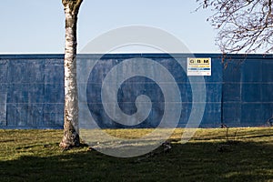 GMB Demolition danger keep out sign on a large blue solid fence wall with grass and a tree in front