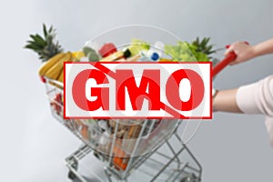 GMO free products. Blurred view of woman with shopping cart full of groceries on grey background