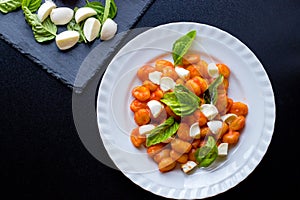 Gnocchi alla Sorrentina in tomato sauce with green fresh basil and mozzarella balls served on a plate photo