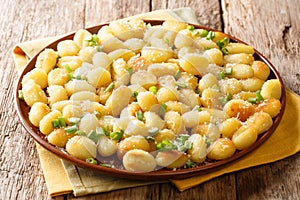 Gnocchi crisped in garlic and green onion infused butter with a generous amount of Parmesan cheese close-up on a plate. Horizontal