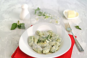 Gnocchi or dumplings with nettle or spinach on a white plate on a light gray background. Served with butter and parmesan cheese