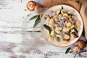 Gnocchi with mushrooms and sage. Above table scene on a rustic white wood background.