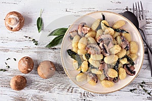 Gnocchi with mushrooms and sage. Top view table scene over rustic white wood.