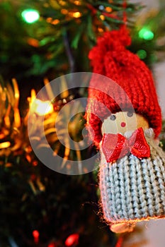 Gnome toy as winter holidays decoration against unfocused new year`s tree with burning festive garland lights.