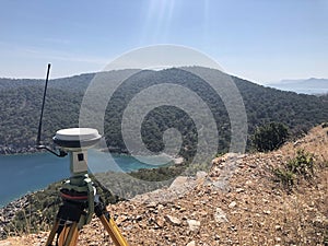 GNSS base receiver stands on the tripod at the hill top against sea at the background photo