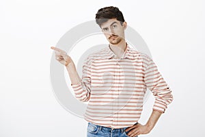 Go away from here, I demand. Studio shot of intrigued handsome male model with moustache, pointing left with index