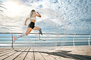 Go. Full-length of young disabled woman with leg prosthesis in sports clothing is running on the bridge