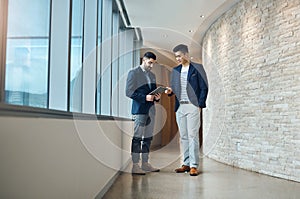 Go with this idea. two young businessmen using a digital tablet together in a modern office.