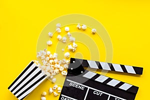 Go to the cinema with popcorn and clapperboard on yellow background top view