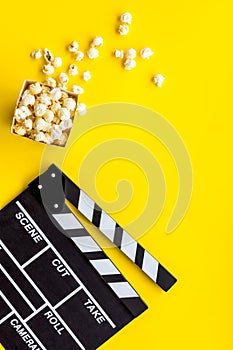 Go to the cinema with popcorn and clapperboard on yellow background top view